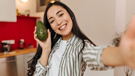 Asian woman holding an avocado takes a selfie