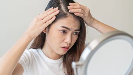 Filipino woman looks at mirror while checking her scalp.