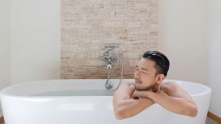 An Asian man relaxing in the bathtub.