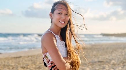 Smiling woman with long straight hair at the beach.