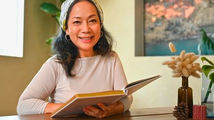 Middle-aged Asian woman reading a book at home.