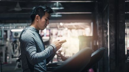 Asian man checking phone on treadmill