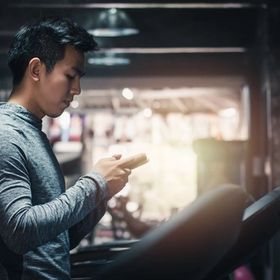 Asian man checking phone on treadmill