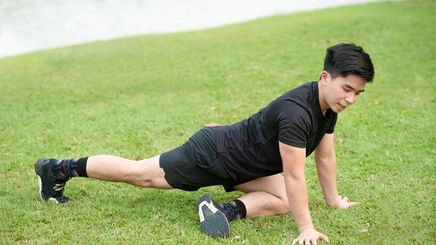 Young Asian man doing a stretching exercise on the grass.