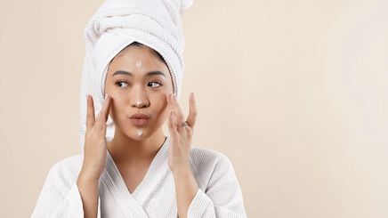 Asian woman in bathrobe and towel applying cream on face
