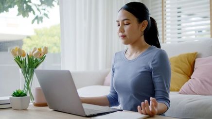 Woman meditating at home in front of her laptop.