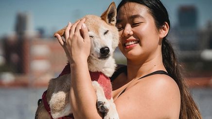 An Asian woman with a ponytail hugging her pet dog