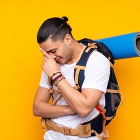 Asian man with backpack and yoga mat against yellow background