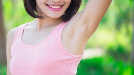 Smiling woman in pink tank top showing one of her underarms.