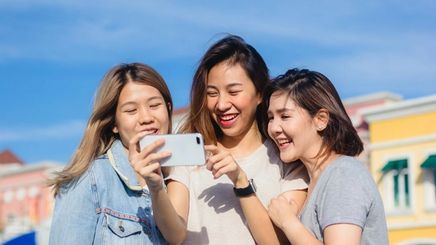 Three happy Asian women looking at a mobile phone.