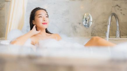 Young Asian woman enjoying a bubble bath with champagne while watching on her iPad. 