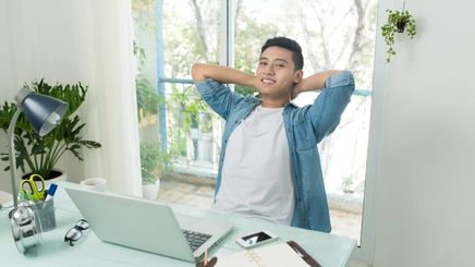 Handsome Asian man leaning back on his desk, with his arms on his neck