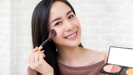 Asian woman applying blush on cheek 
