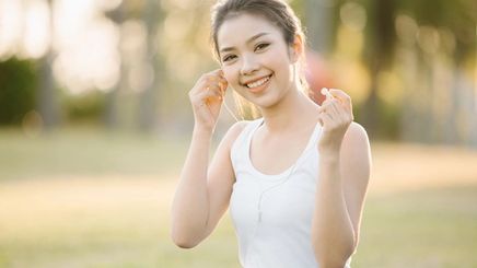 A happy young Asian woman putting on her earphones outdoors.