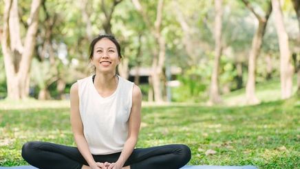 Happy Asian woman sitting on a yoga mat outdoors.