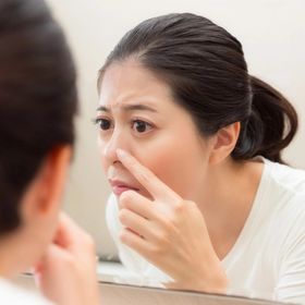 Asian woman touching nose in the mirror.