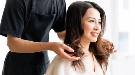 Asian woman happily getting her hair styled at a salon.