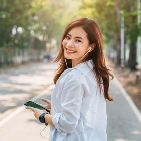 Asian woman wearing earphones, smiling, walking outdoors