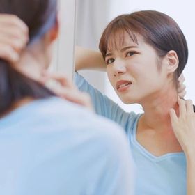 Asian woman in a blue shirt scratching itchy skin on her neck