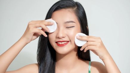 A young Asian girl holding cotton pads to her face.