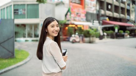 Asian woman with long healthy hair smiling with her back turned.