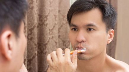 Asian man brushing teeth with orange toothbrush