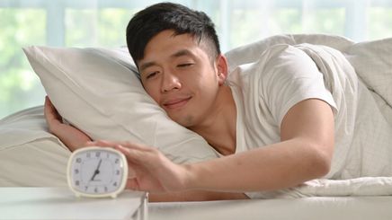 Man waking up and turning off his alarm clock on his side of the bed.