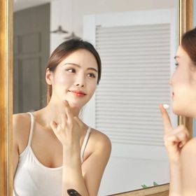 Asian woman applying product while looking in a mirror. 
