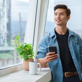 Man looking at holding his phone while looking out a window. 
