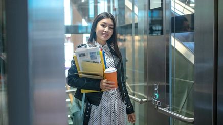 Asian woman carrying files and coffee in an elevator