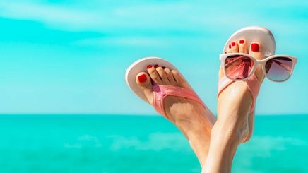 Closeup of sunglasses and feet wearing sandals with the ocean in the background