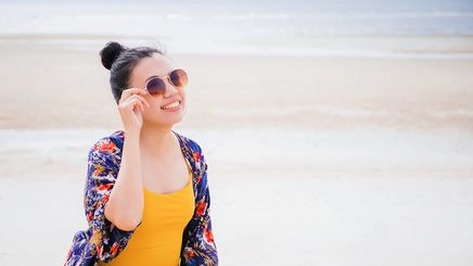 A female tourist walking on a beach and wearing sunglasses