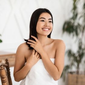 Asian woman sitting and touching her hair while smiling  
