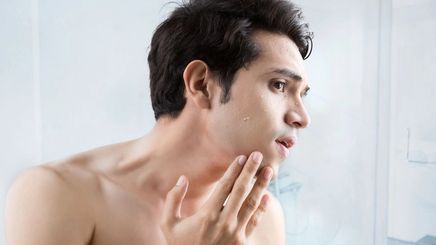 Filipino man touches his face, looks at skin in the mirror.