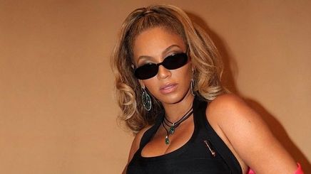 Beyoncé wearing curly ponytail, black sunnies, little black dress, and pink coat.
