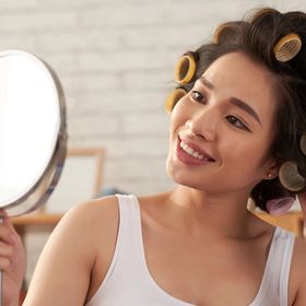 Smiling woman wearing hair rollers looking at her reflection in the mirror.