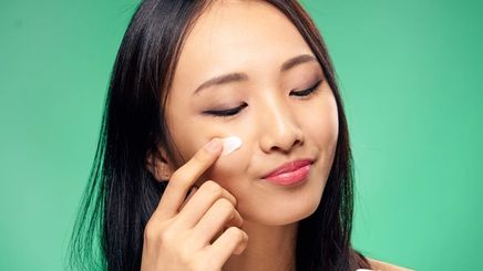 An Asian woman applying a cream under her eyes