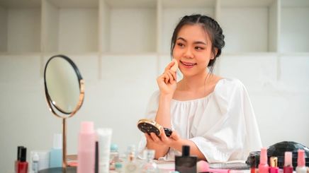 Woman applying cushion foundation while sitting in front of a vanity table.