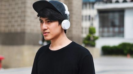 Asian man with bangs wearing a black cap and white headphones.