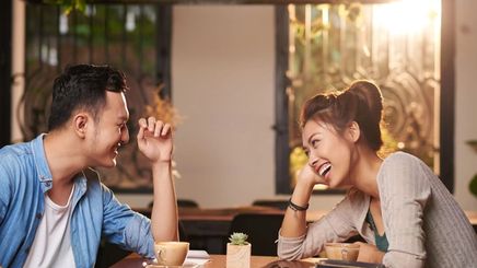 Man and woman laughing while talking as they sit a wooden table in a café 