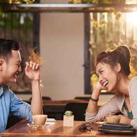 Man and woman laughing while talking as they sit a wooden table in a café 