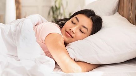 Woman is sleeping comfortably on her bed with white pillows and sheets. 