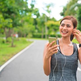 Asian woman wearing earphones while jogging outside.