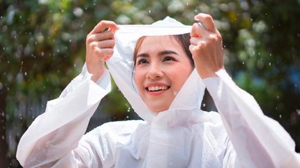 Woman in white raincoat smiling while standing in the rain.