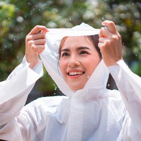 Woman in white raincoat smiling while standing in the rain.