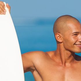 Young man with a shaved head holding a surfboard on the beach