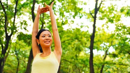 Asian woman in a yellow top stretching outdoors.