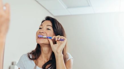 Woman looking at the mirror brushing her teeth with a toothpaste.