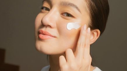 Asian woman applying sunscreen on her cheek.