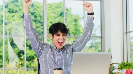 Asian man raising arms in front of laptop